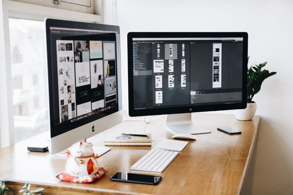 Web design workspace with monitors displaying website layouts and design work